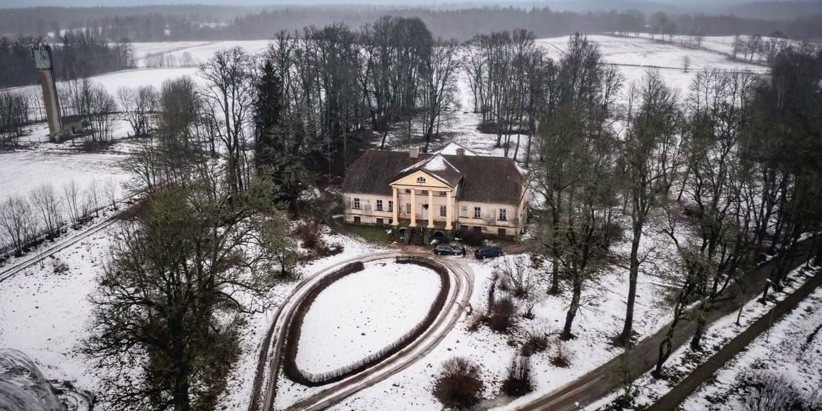 Aerial view of a historic mansion amidst a snowy landscape in Latvia, captured from above.