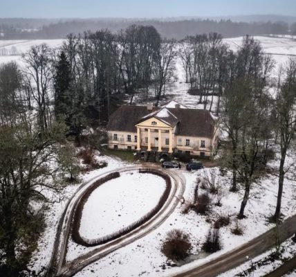 Aerial view of a historic mansion amidst a snowy landscape in Latvia, captured from above.