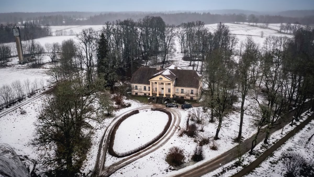Aerial view of a historic mansion amidst a snowy landscape in Latvia, captured from above.